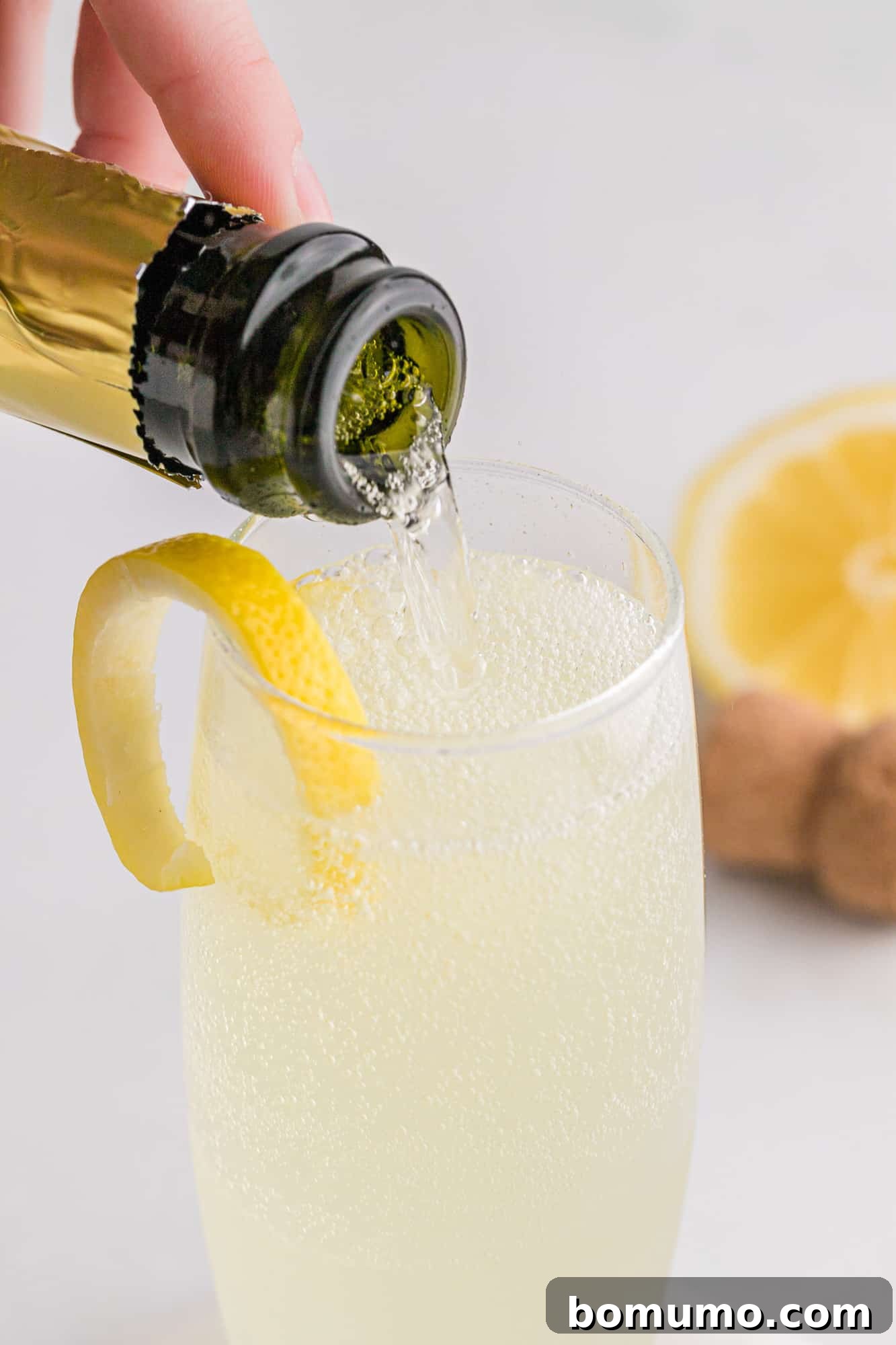 A bottle of prosecco or sparkling wine being carefully poured into a champagne flute already partially filled with the French 75 mixture, adding the final effervescent touch and creating beautiful bubbles.