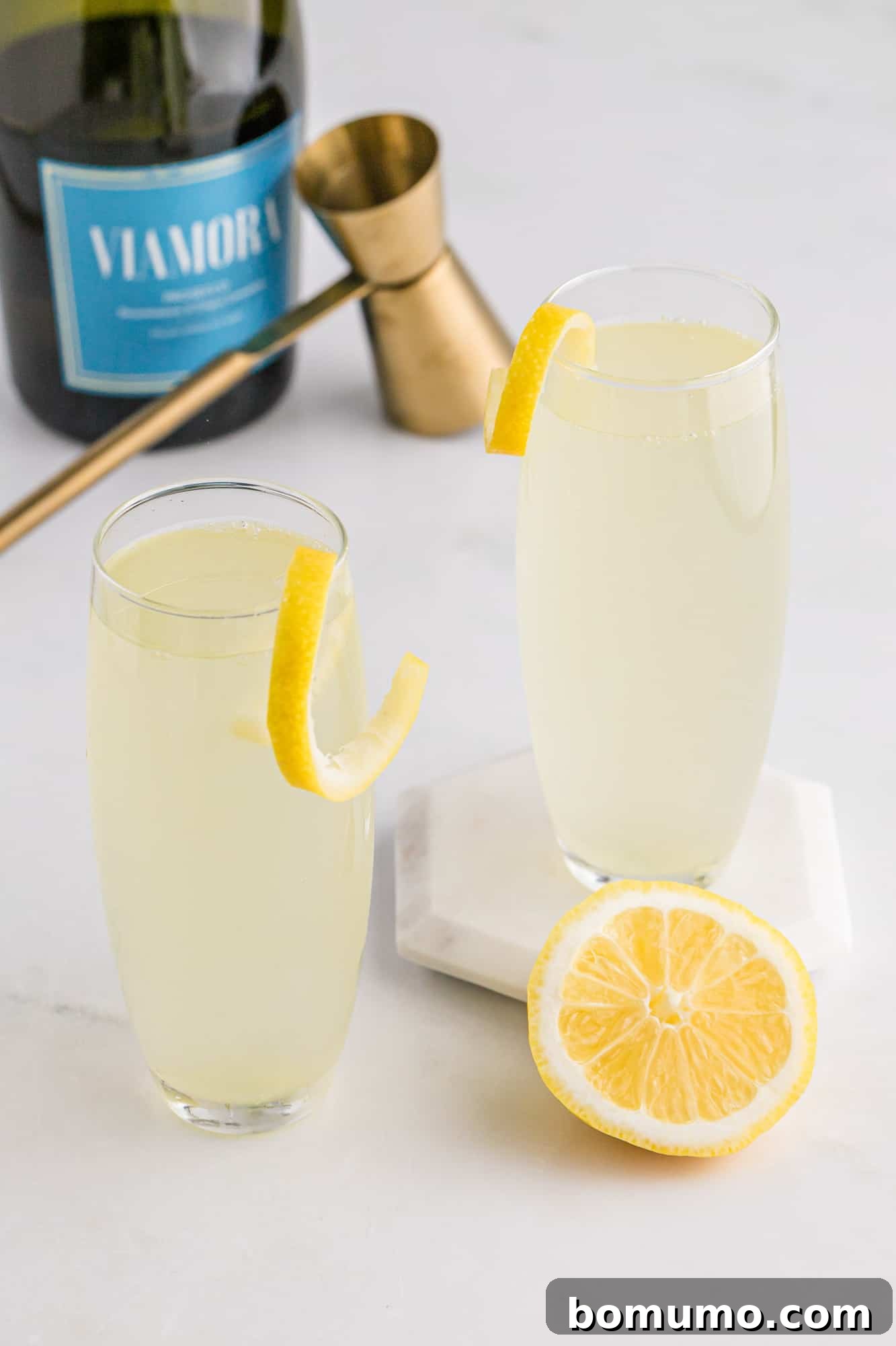 Two sparkling wine cocktails, possibly French 75s, in elegant stemless flutes, with a softly blurred background that hints at a festive gathering or sophisticated bar setting, emphasizing the celebratory mood.