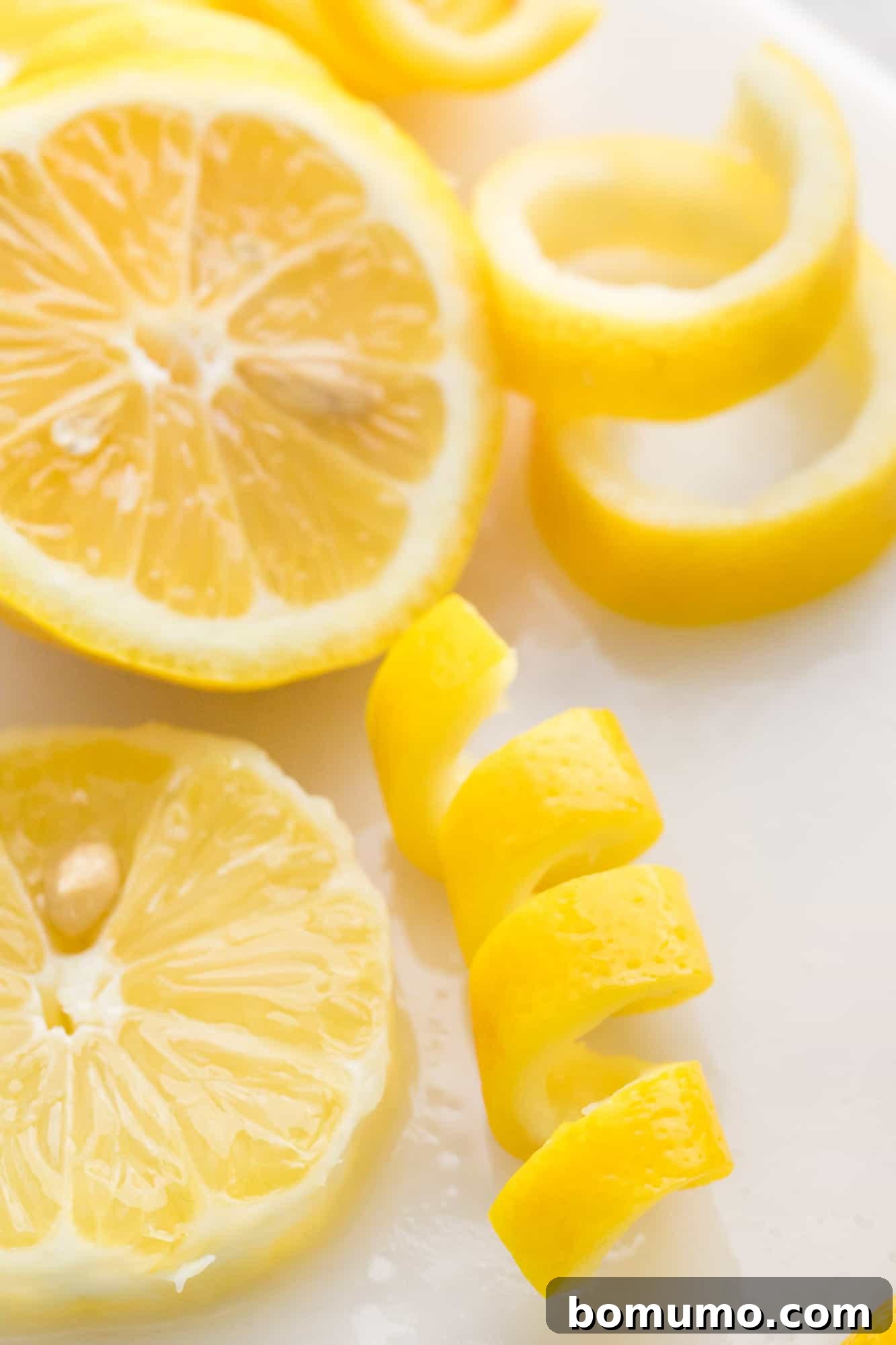 A neatly spiraled lemon peel, ready for garnishing, rests beside several fresh lemon rounds, emphasizing the importance of fresh citrus in cocktail preparation and presentation.