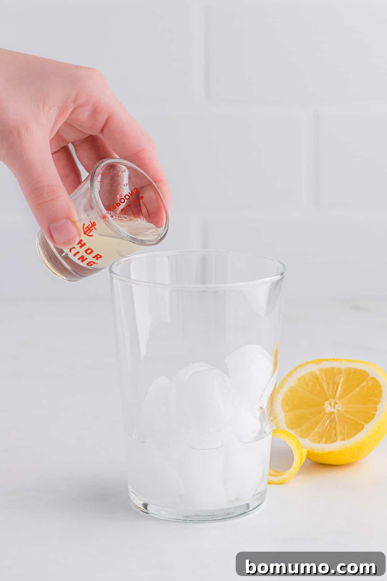 Freshly squeezed lemon juice being carefully poured into a cocktail shaker already containing other ingredients, demonstrating the precision involved in mixing a French 75.