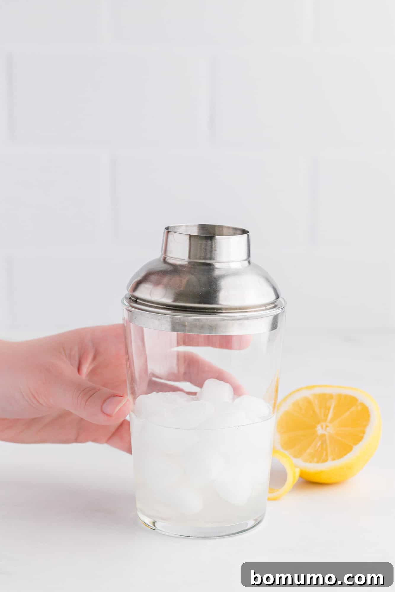 A metal cocktail shaker, filled with ice and liquid ingredients, held mid-shake, conveying the action needed to thoroughly chill and mix the components of the French 75 cocktail.