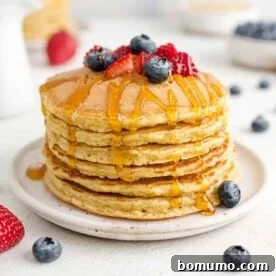 A tempting stack of quinoa pancakes, elegantly topped with fresh mixed berries and a generous drizzle of golden syrup.
