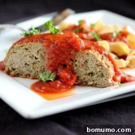 A generous serving of Italian Turkey Quinoa Meatloaf on a white plate, accompanied by a side of noodles and marinara sauce.