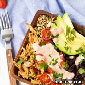 A delicious southwestern quinoa bowl with chicken, served in a square wooden salad bowl, with a fork resting alongside.