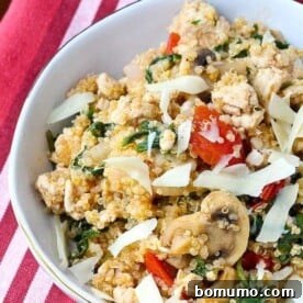 An overhead view of a colorful quinoa dish with ground turkey, kale, mushrooms, and tomatoes, served in a round white dish.