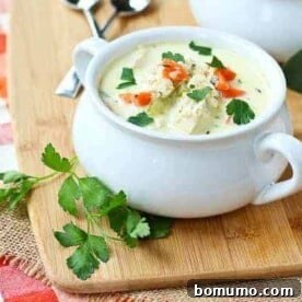 A warm serving of creamy turkey soup with quinoa, garnished with fresh chopped parsley, in a white bowl.