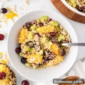 A refreshing quinoa salad, vibrant with segments of juicy orange and plump red grapes, served beautifully in a white bowl.
