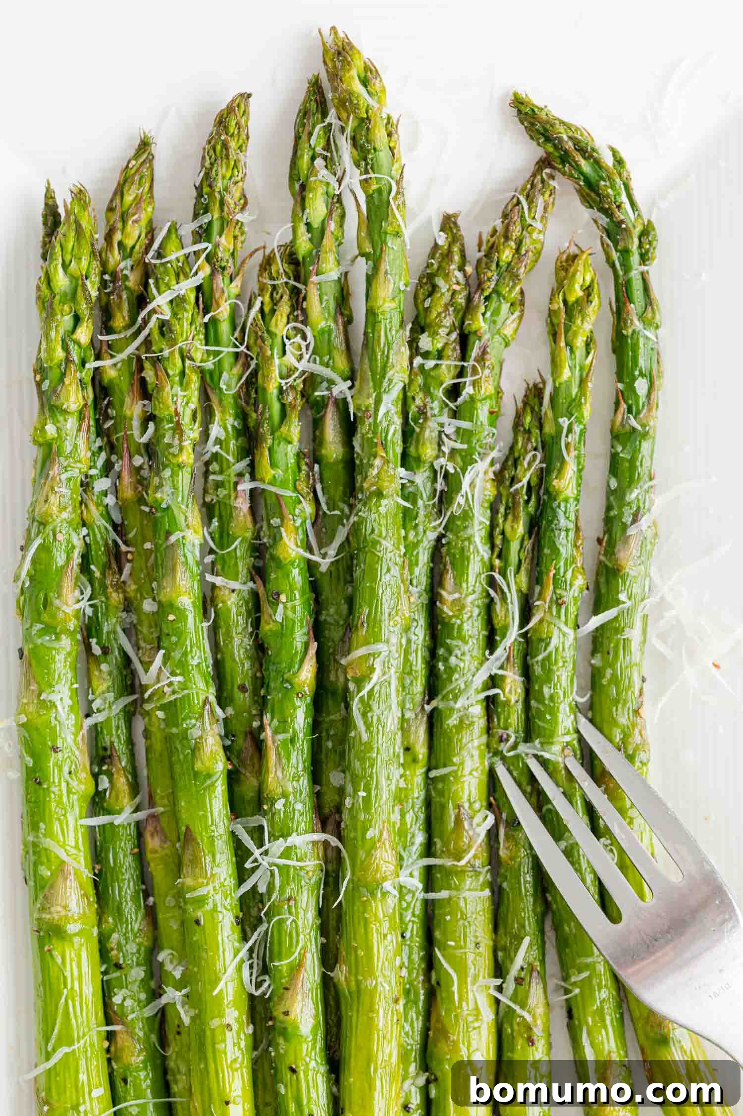 Crisp air fryer asparagus spears served with grated Parmesan cheese and a fork, emphasizing its gourmet appeal and delicious readiness.