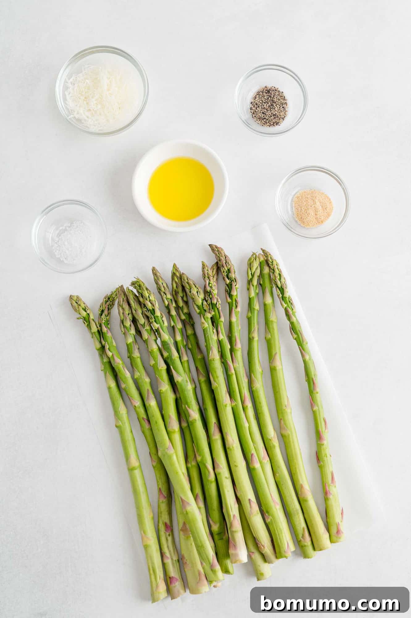 Fresh green asparagus spears, a bottle of olive oil, salt, and pepper shakers neatly arranged, showcasing the simple ingredients needed for this easy and healthy air fryer recipe.