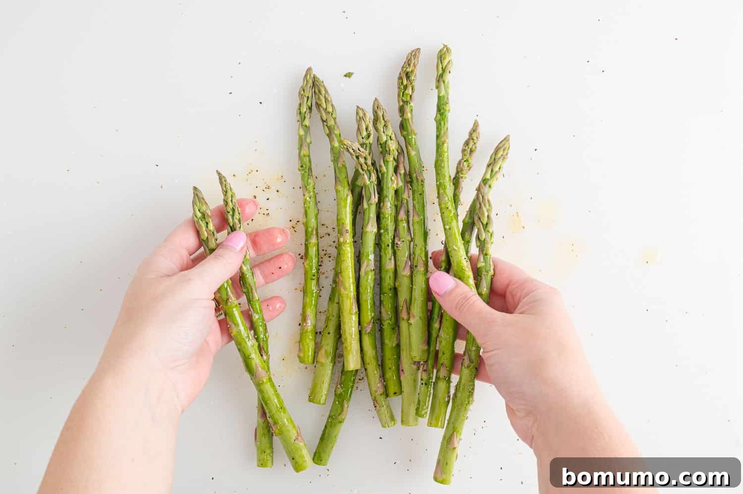 Asparagus spears being tossed with olive oil and seasonings in a bowl, ensuring an even coat before air frying for maximum flavor.