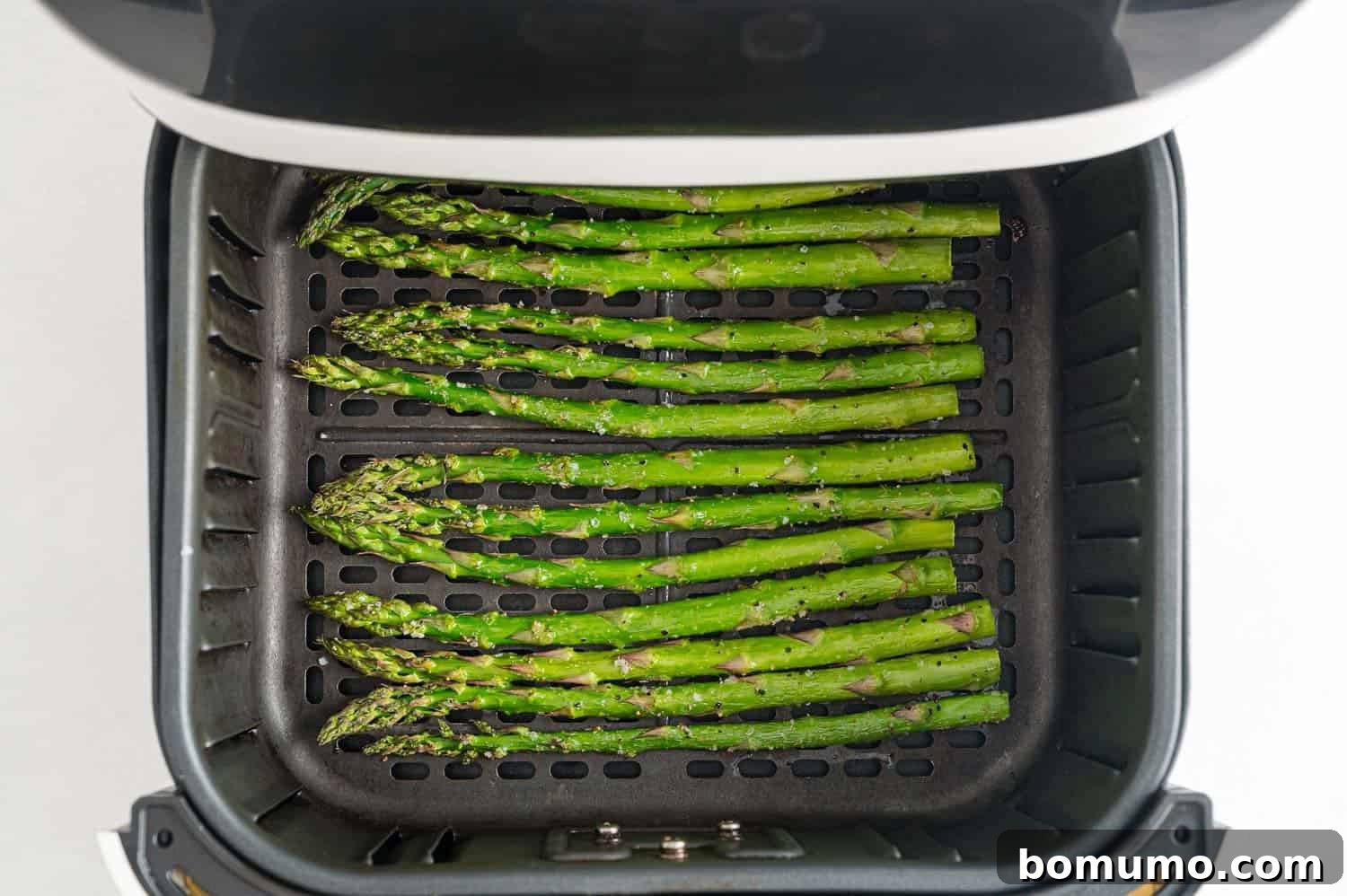 Perfectly cooked, vibrantly green asparagus spears hot in the air fryer basket after being air-fried to a crisp-tender finish, ready to serve.