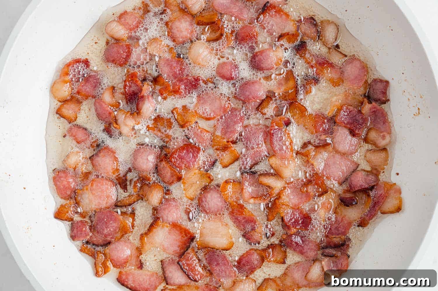 Bacon cooking in frying pan. Small pieces of bacon sizzling in a cast iron skillet.