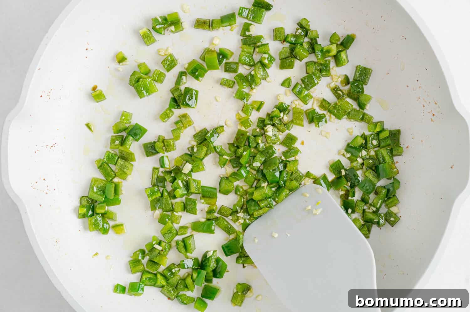 Diced jalapeño in a frying pan. Bright green jalapeño pieces being cooked in a dark skillet.