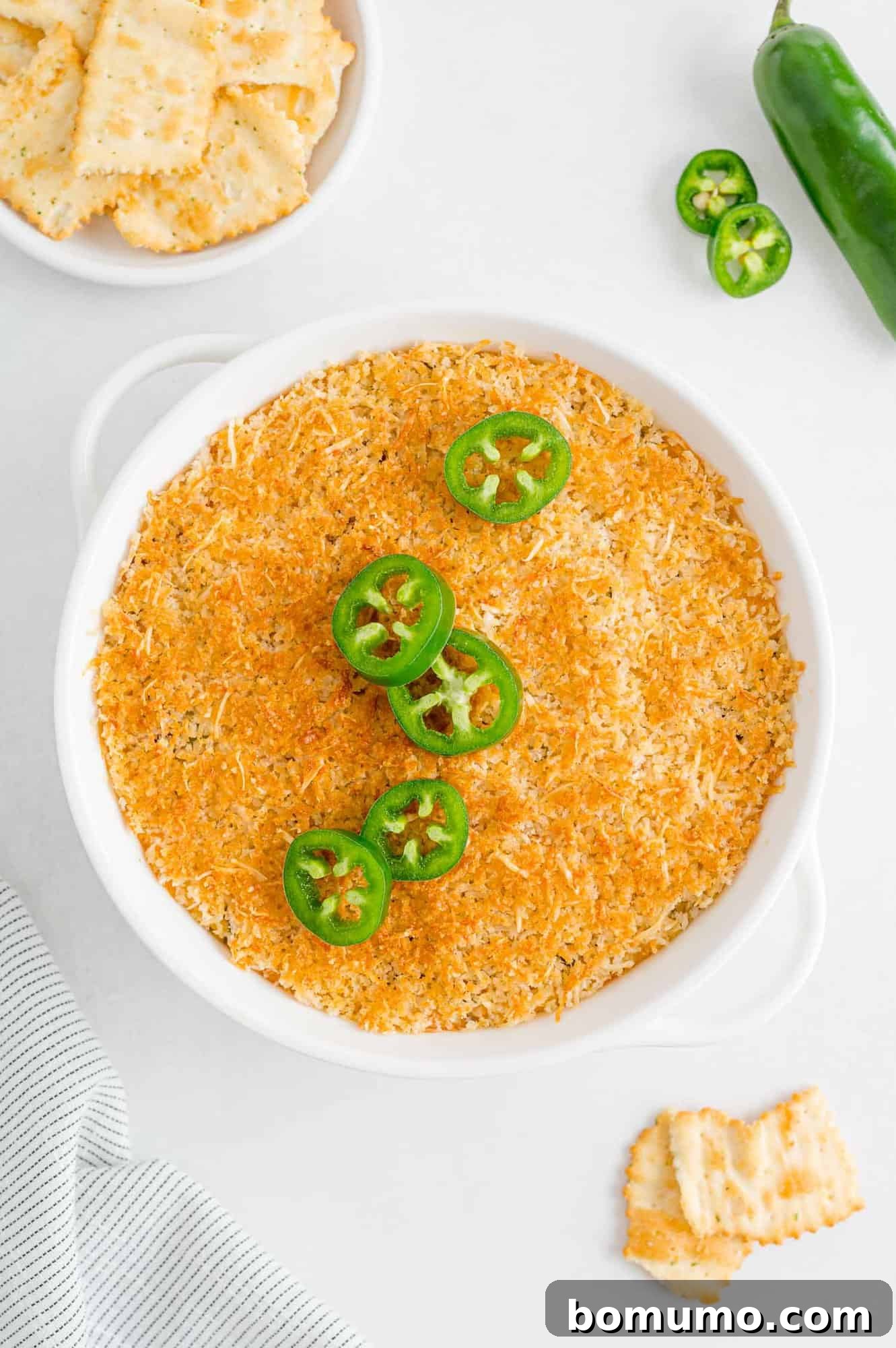 Baked dip topped with sliced jalapeño peppers. A close-up of the finished dip, garnished with fresh green jalapeño slices.