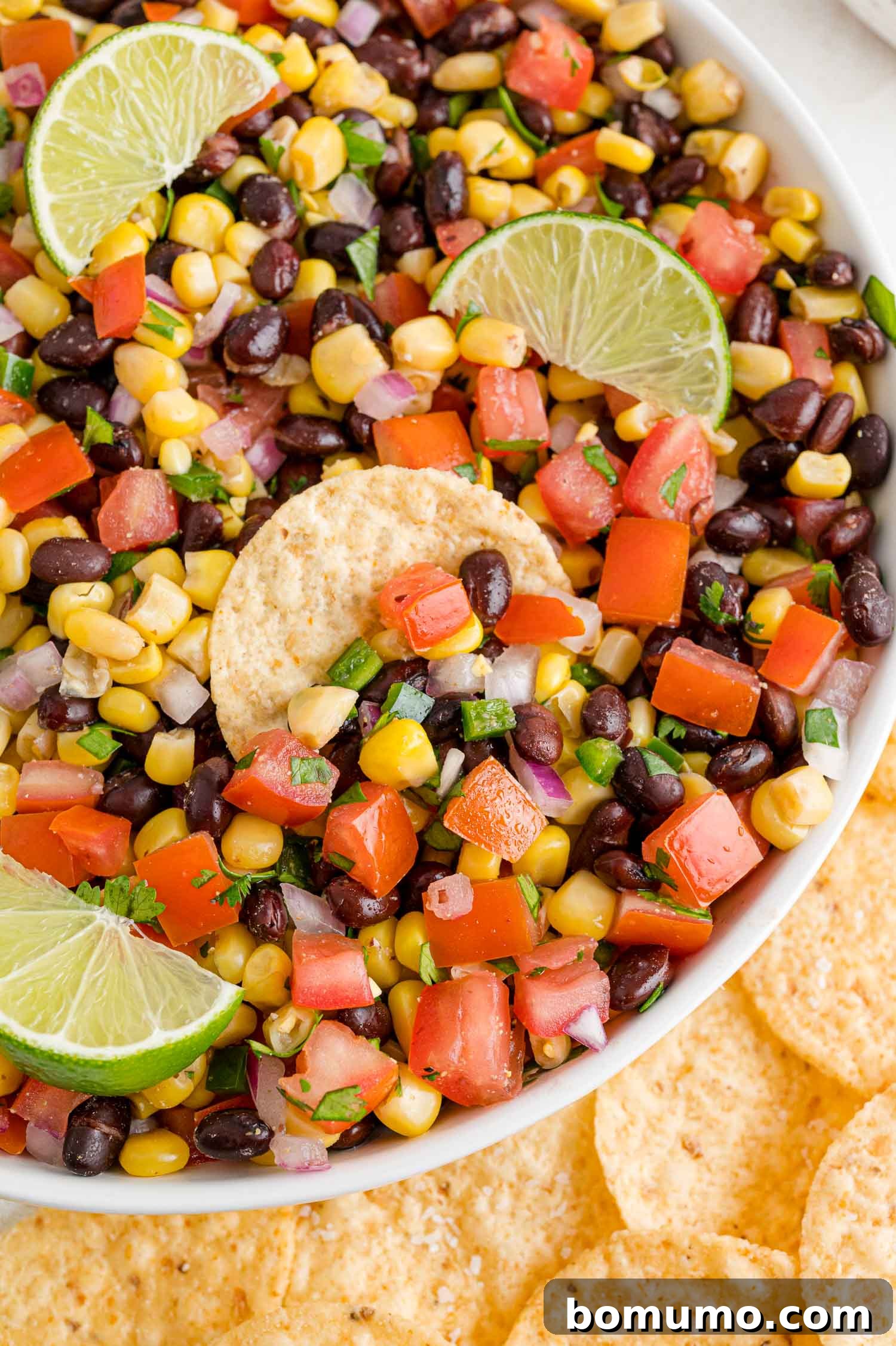 Fiesta Black Bean Corn Salsa 2 A vibrant bowl of black bean corn salsa, garnished with a tortilla chip and fresh lime wedges, ready to be enjoyed.