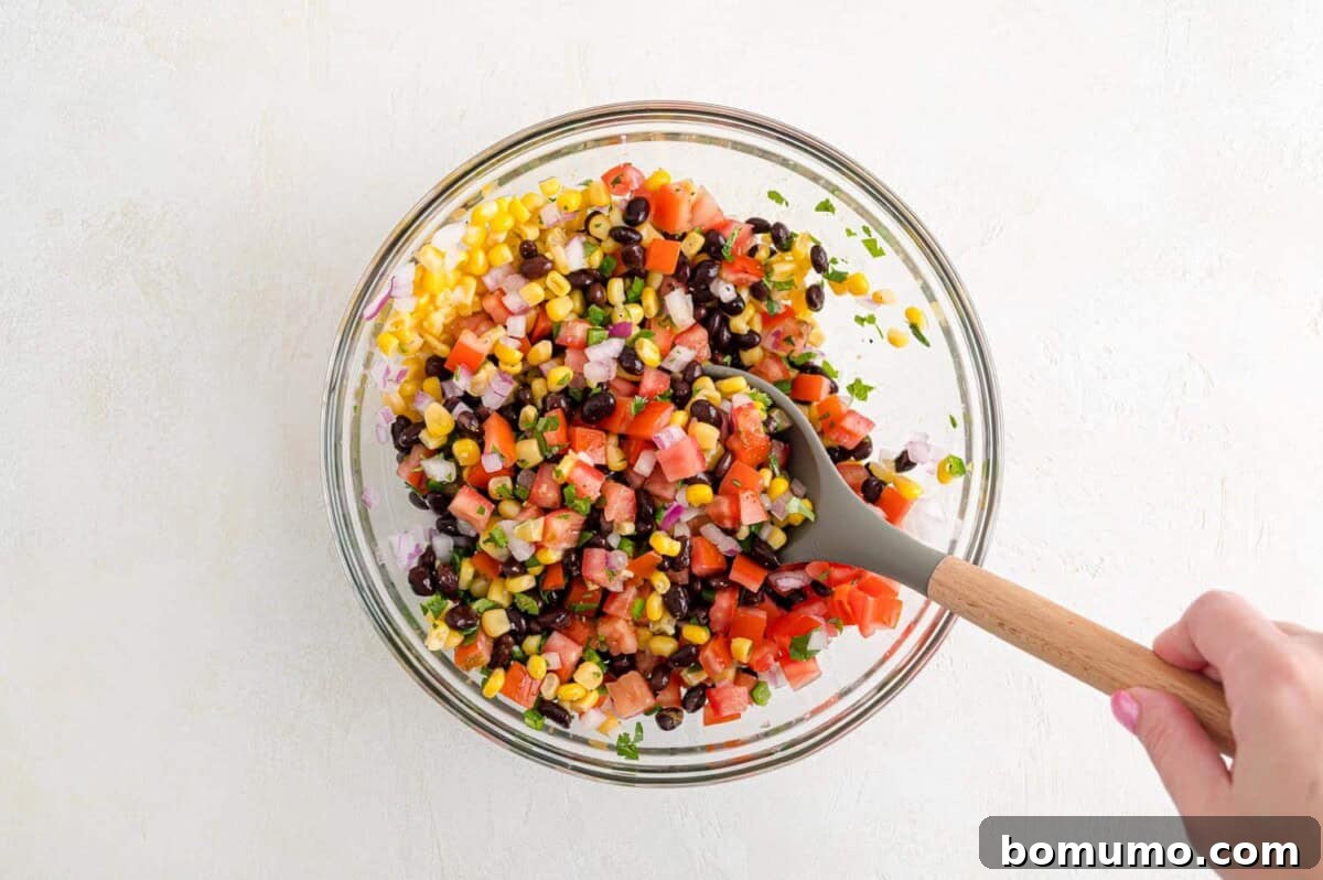 Fiesta Black Bean Corn Salsa 6 A hand stirring the colorful black bean corn salsa in a mixing bowl, showcasing the fresh ingredients mingling.