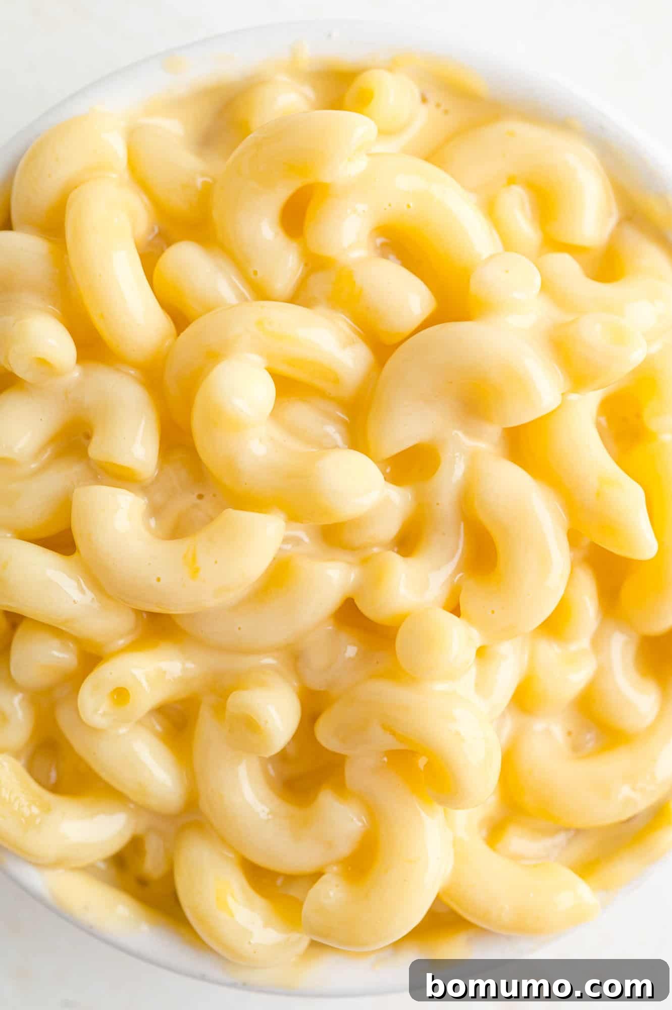 Close up of perfectly cooked, creamy macaroni and cheese in a white bowl, ready to be enjoyed.