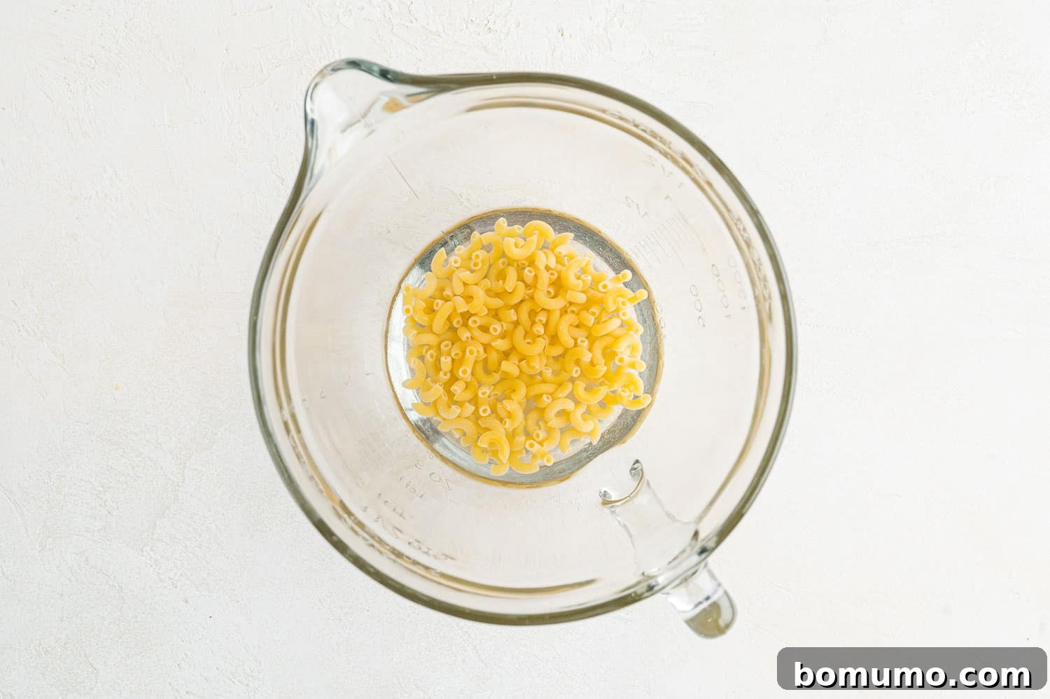 Uncooked elbow macaroni and water in a microwave-safe bowl, ready for cooking.
