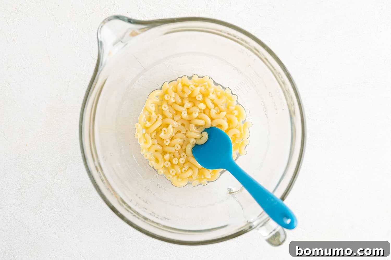 Partially cooked macaroni pasta in a large bowl after microwave cooking, with most water absorbed.