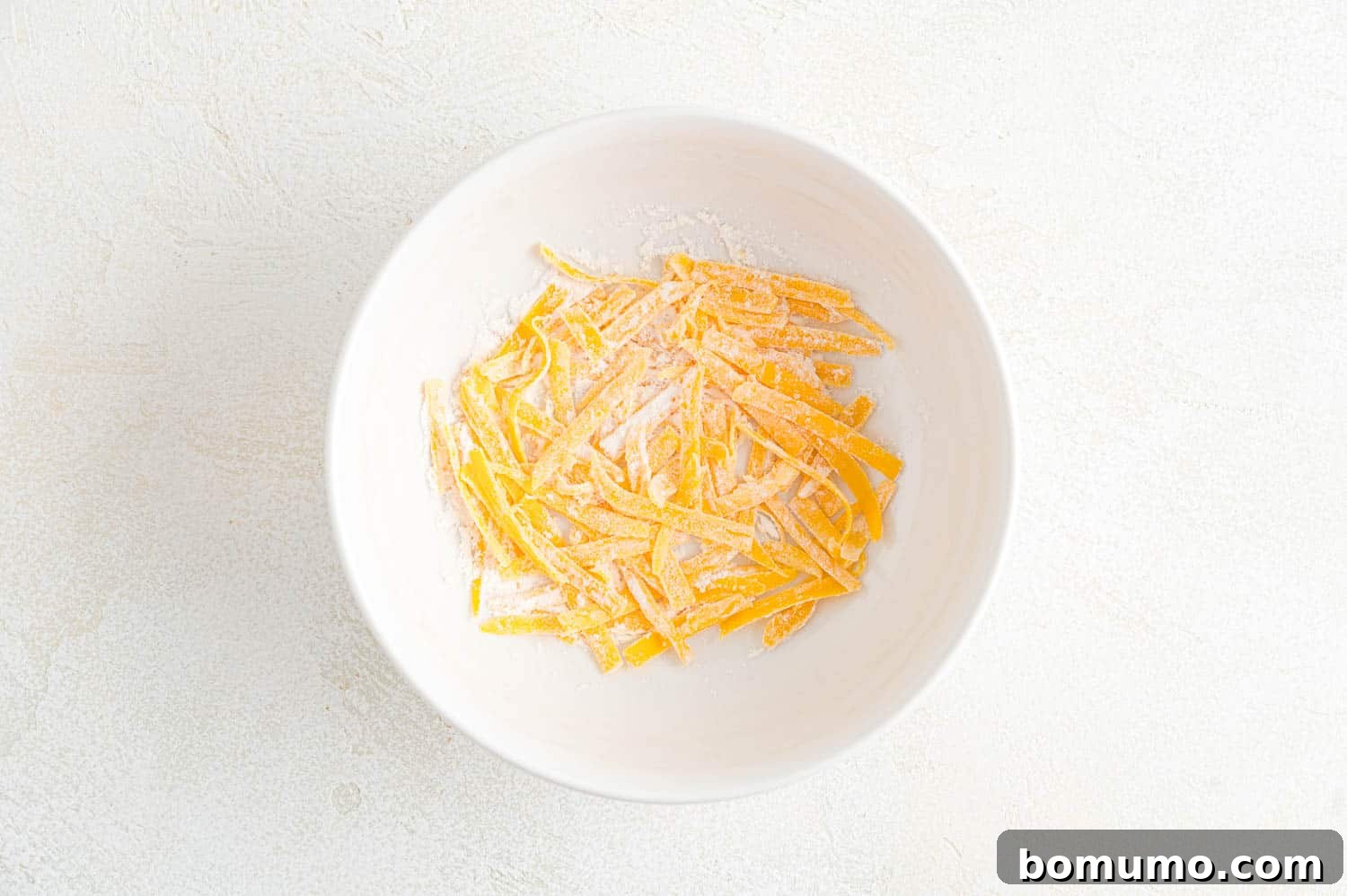 Shredded cheddar cheese tossed with flour in a bowl, prepared for the mac and cheese sauce.