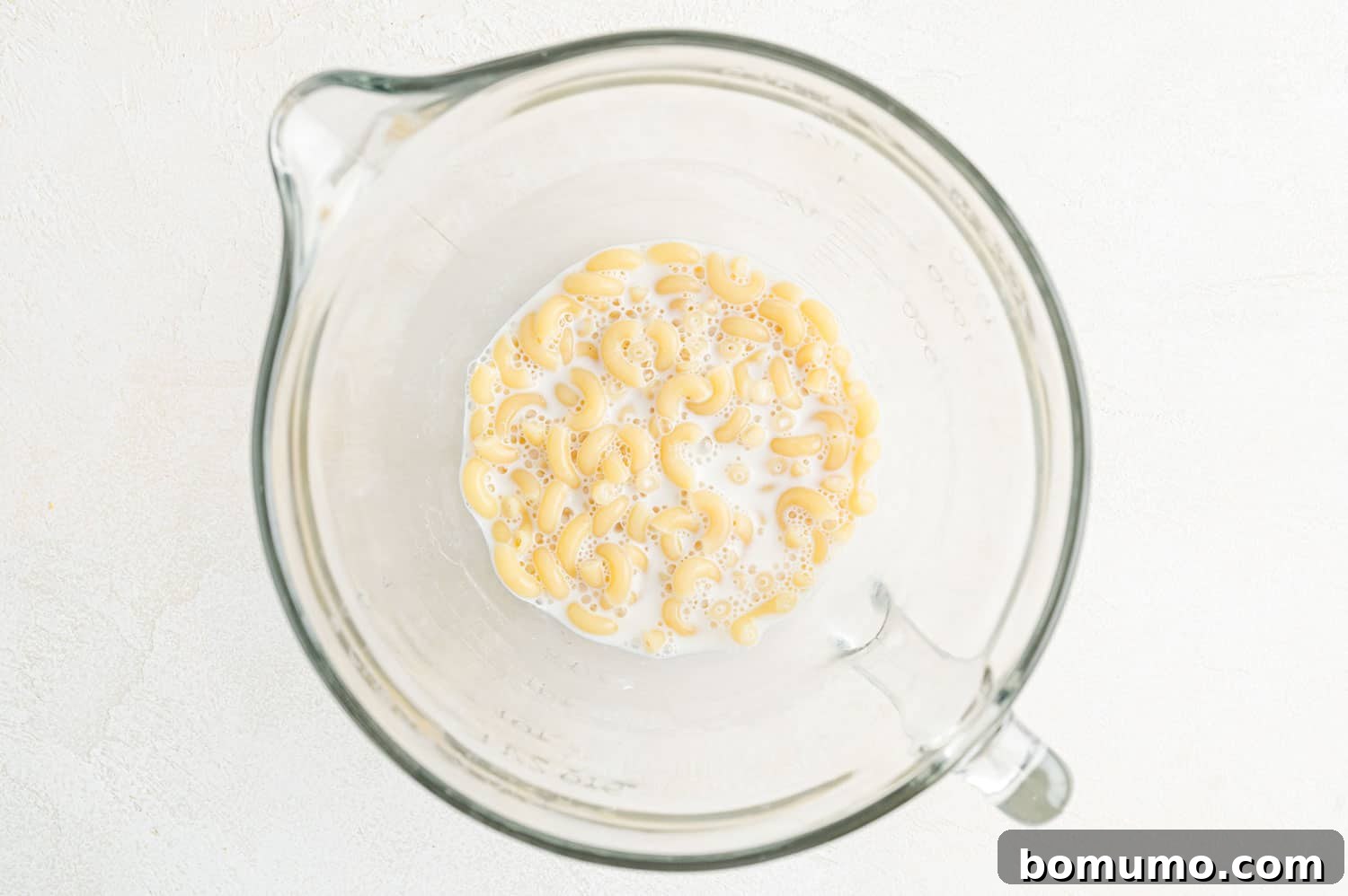 Whole milk mixed with cooked macaroni in a measuring cup, ready for the next step.