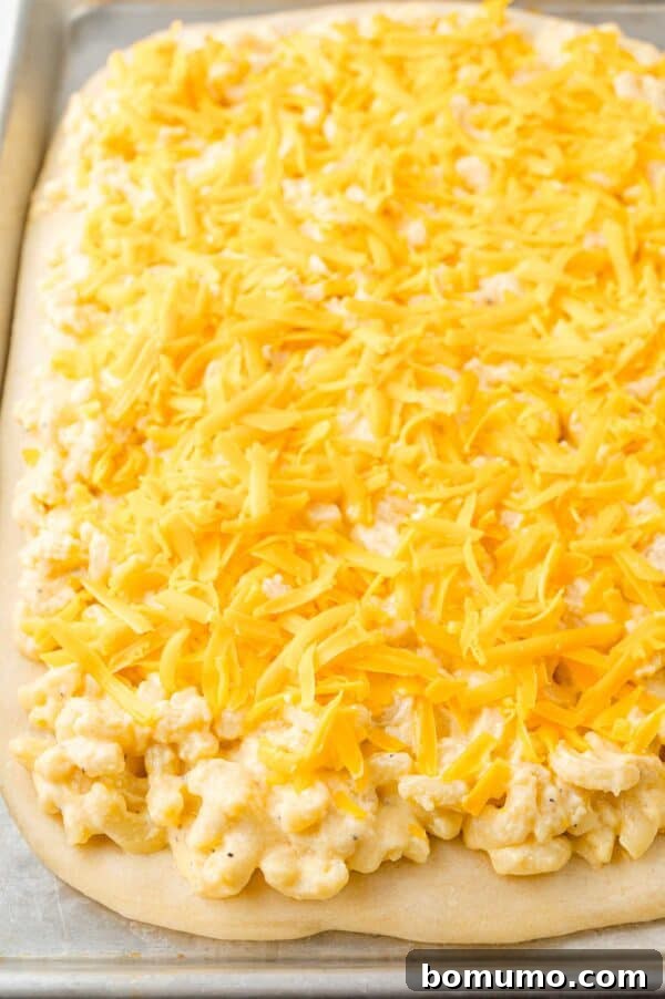 Ultimate Comfort Pizza 11 An extra layer of shredded cheese sprinkled over the macaroni and cheese topping on the pizza, ready for baking.