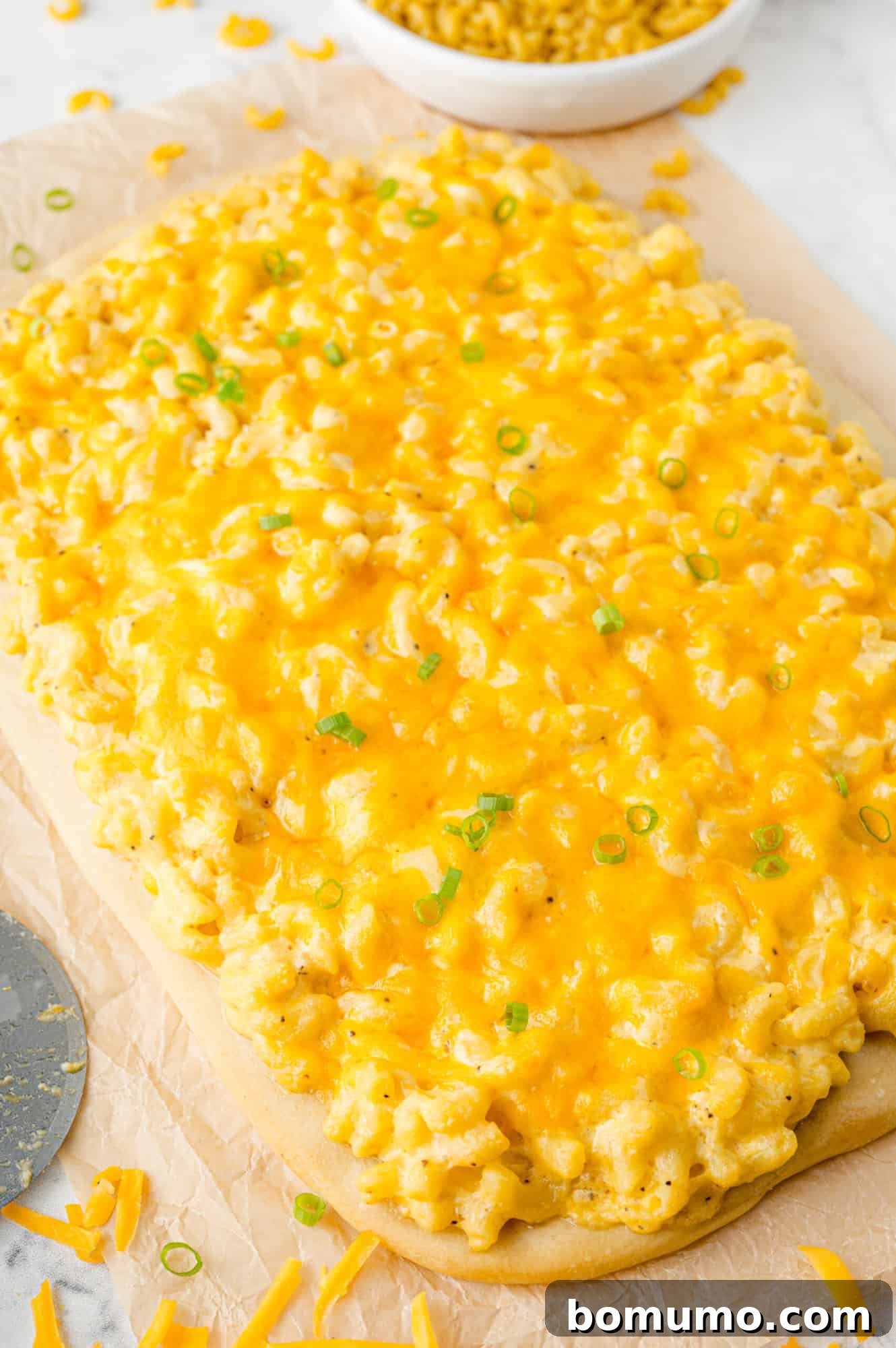 Ultimate Comfort Pizza 12 A whole, unsliced mac and cheese pizza fresh out of the oven, topped with vibrant green onions, ready to be cut and served.
