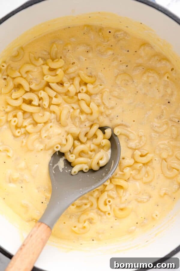 Ultimate Comfort Pizza 7 Cooked pasta being gently stirred into a rich, creamy cheese sauce, ensuring every piece is coated.