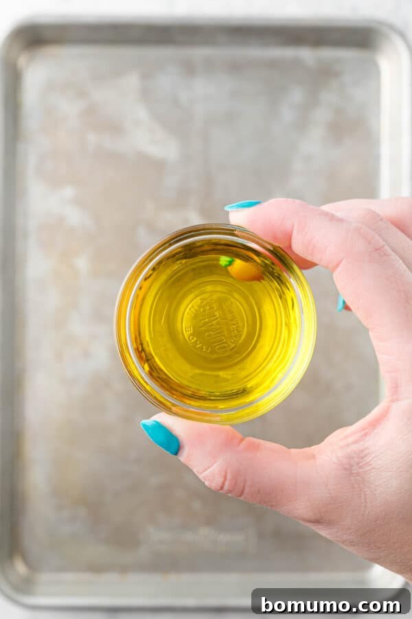 Ultimate Comfort Pizza 8 A hand holding a bottle of olive oil, drizzling it onto a sheet pan to grease the surface for pizza dough.