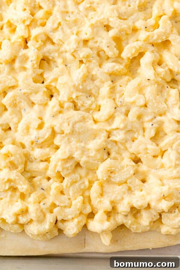 Ultimate Comfort Pizza 10 Creamy macaroni and cheese being spread generously over a pre-baked pizza crust on a sheet pan.