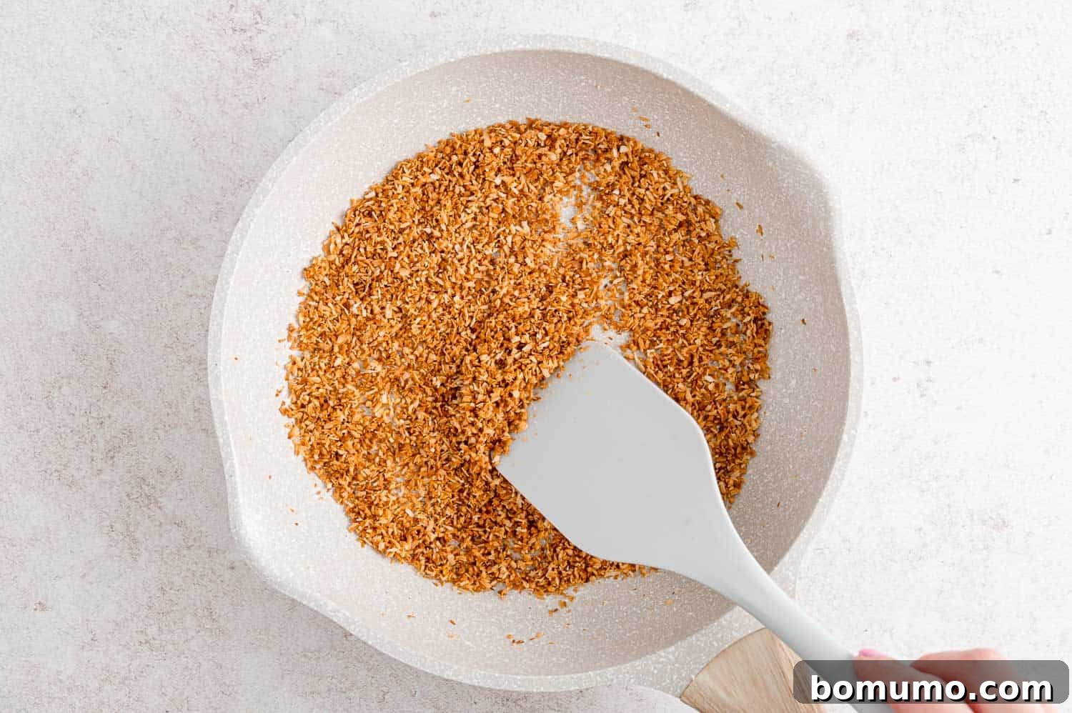 Tropical Coconut Bliss 5 Unsweetened shredded coconut being toasted to a golden brown in a white frying pan.