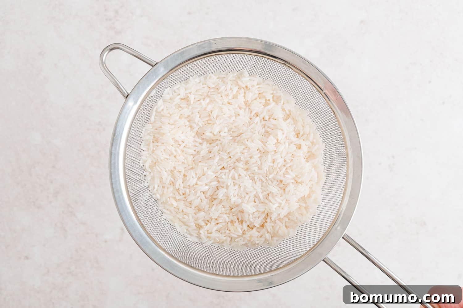 Tropical Coconut Bliss 6 Fragrant jasmine rice being rinsed in a fine mesh strainer under cool water.