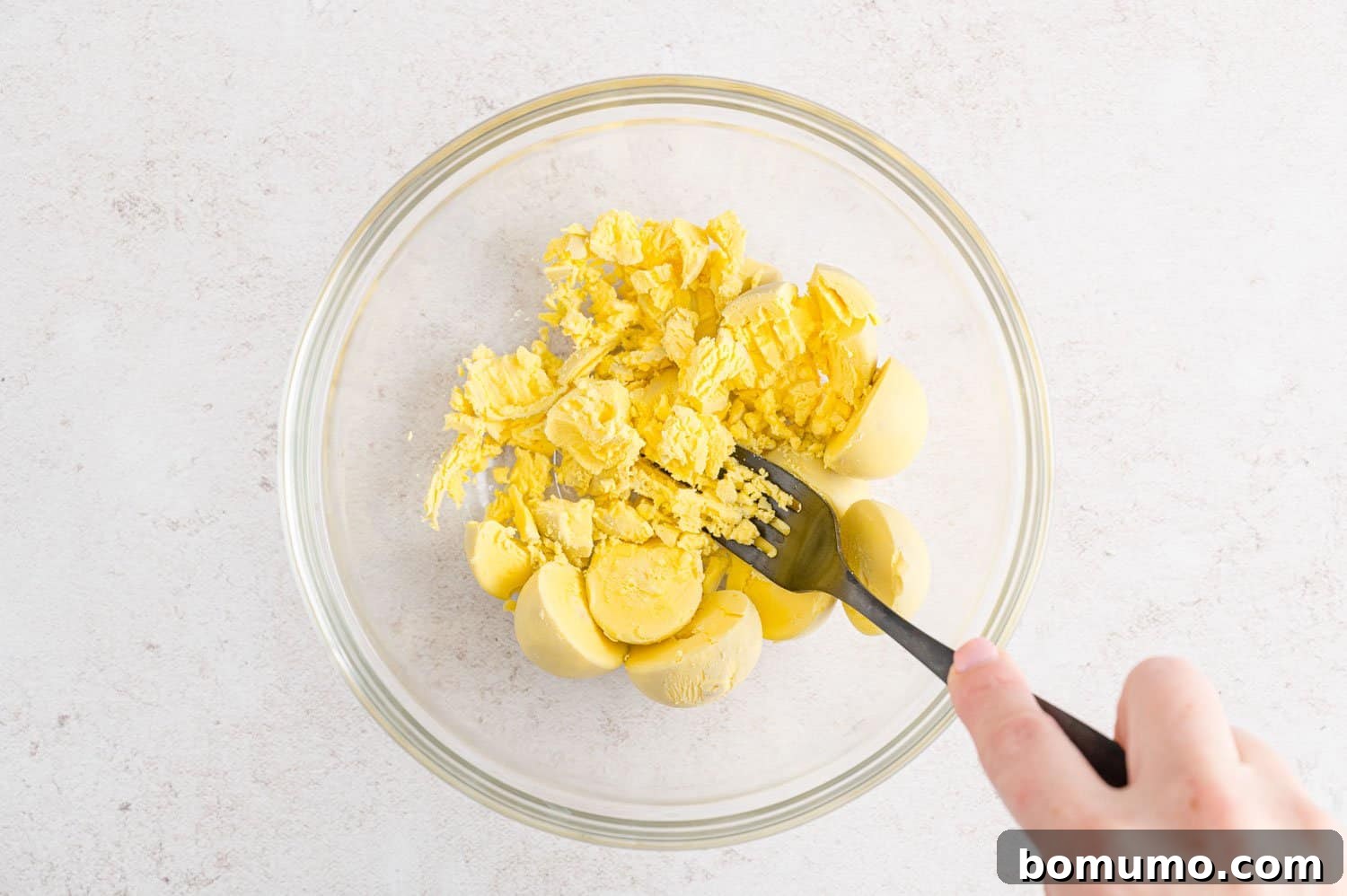 Egg yolks in a bowl, being mashed with a fork.
