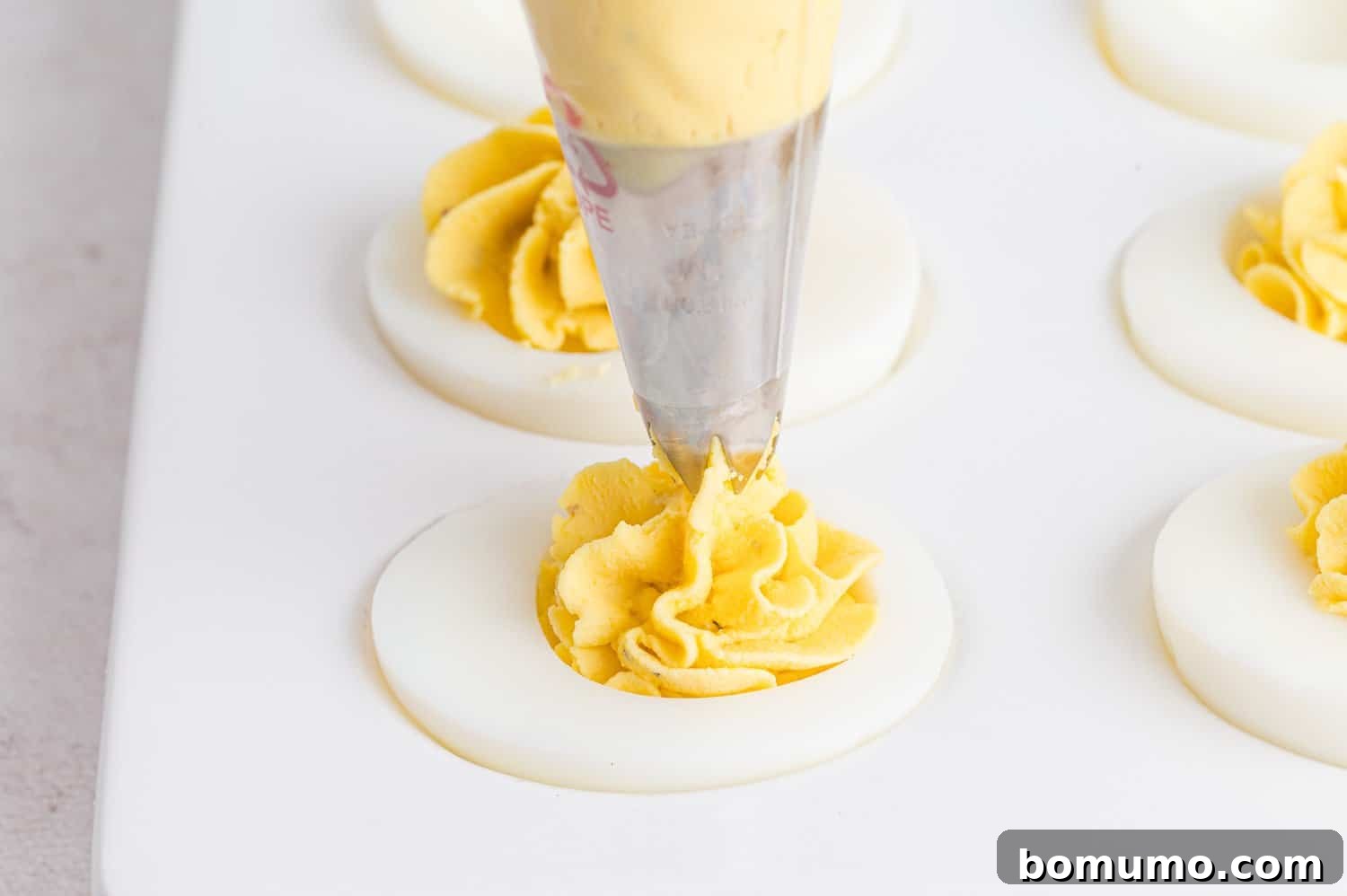 Deviled eggs being filled with a piping bag.