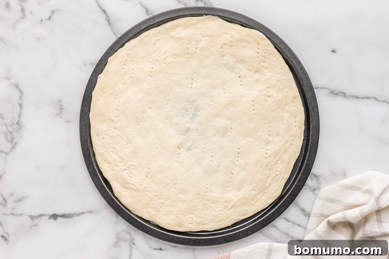 A pristine, uncooked pizza dough stretched and ready on a baking sheet, awaiting its delicious toppings.