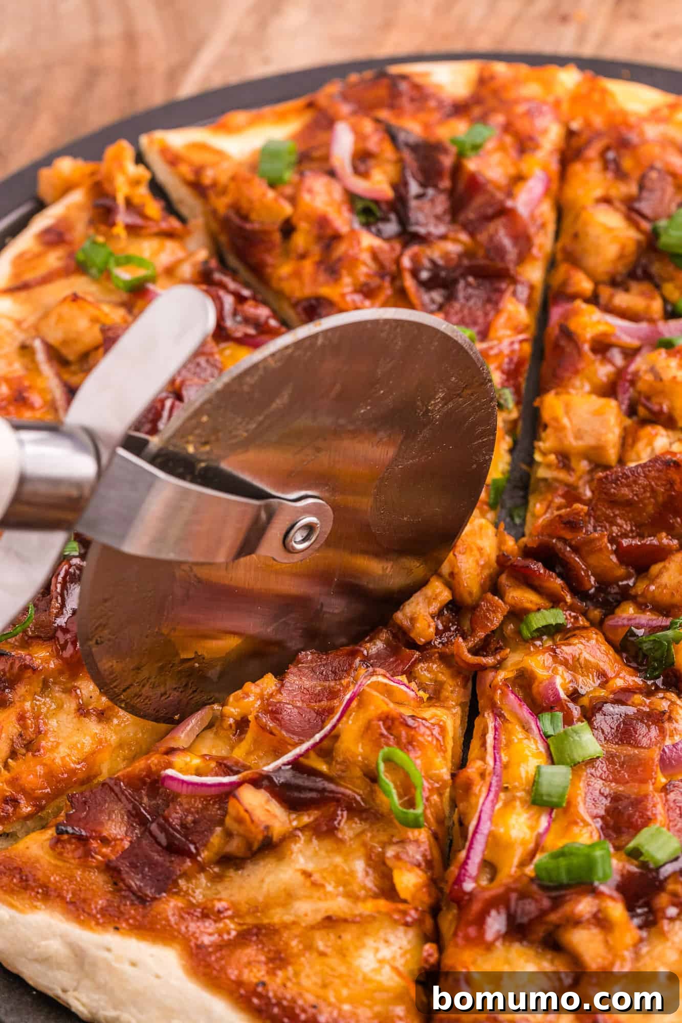 A freshly baked BBQ chicken pizza being expertly sliced into individual portions with a pizza cutter, ready to be served.