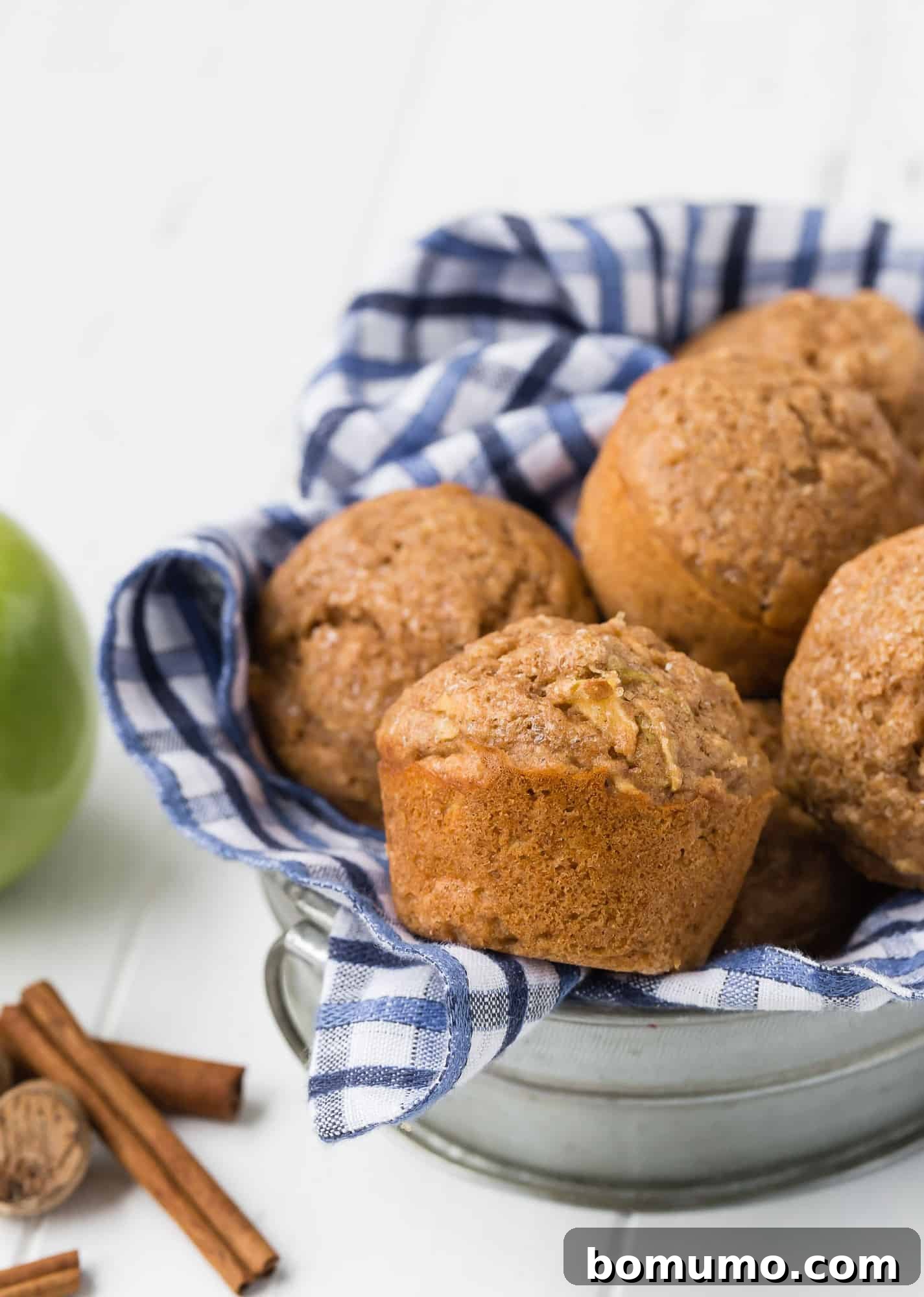 Whole wheat apple muffins in a metal basket with a blue and white checkered towel.