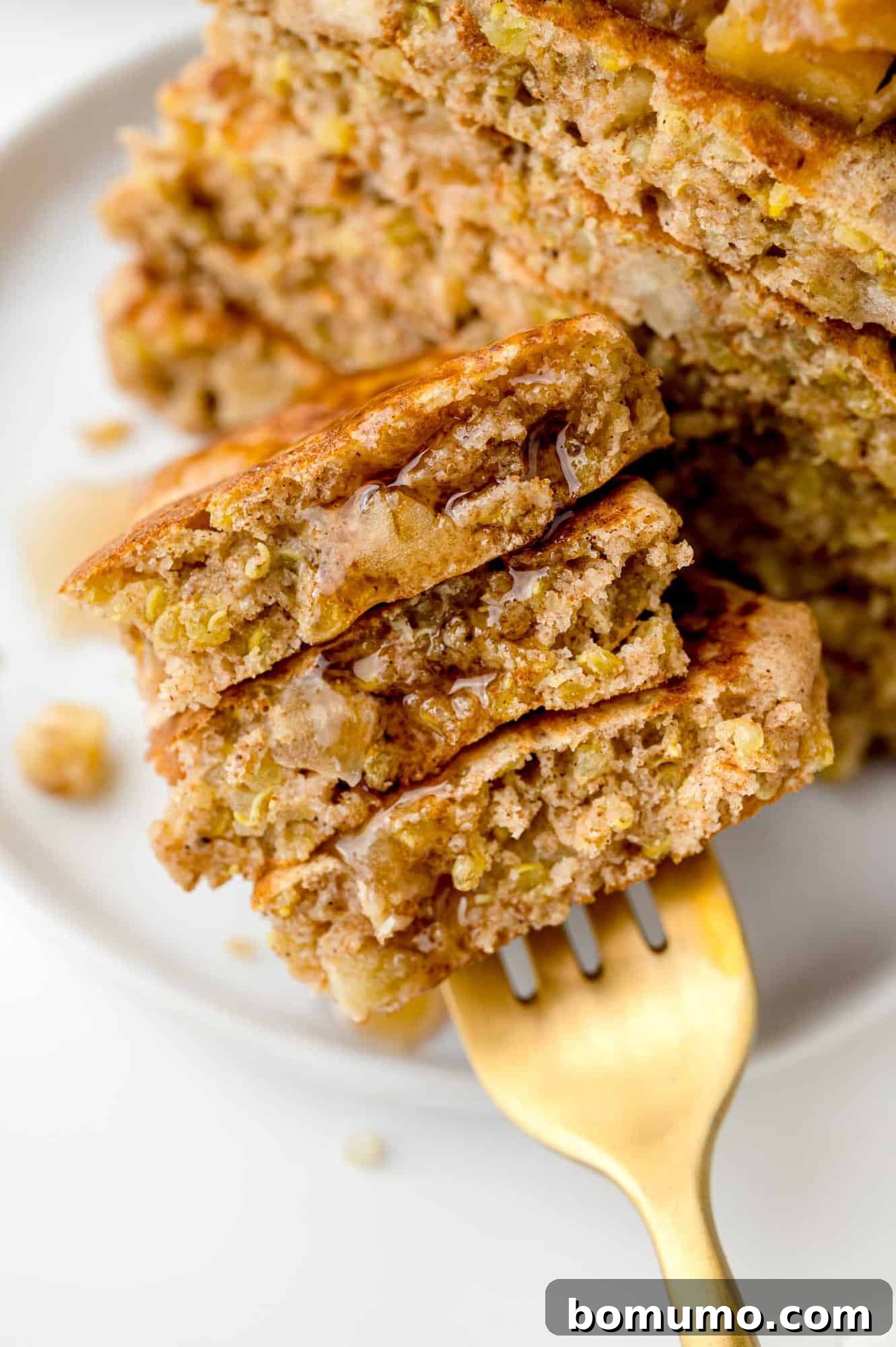 Apple quinoa pancakes on a fork with syrup, emphasizing their delicious appeal.