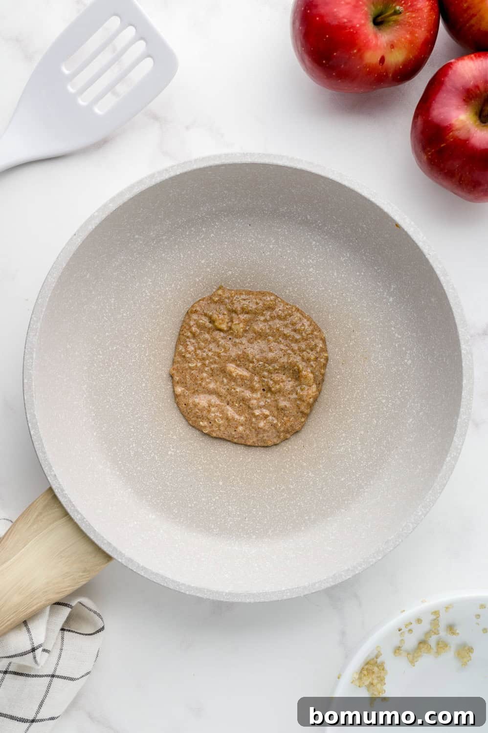 An uncooked apple quinoa pancake portion sizzling on the griddle.