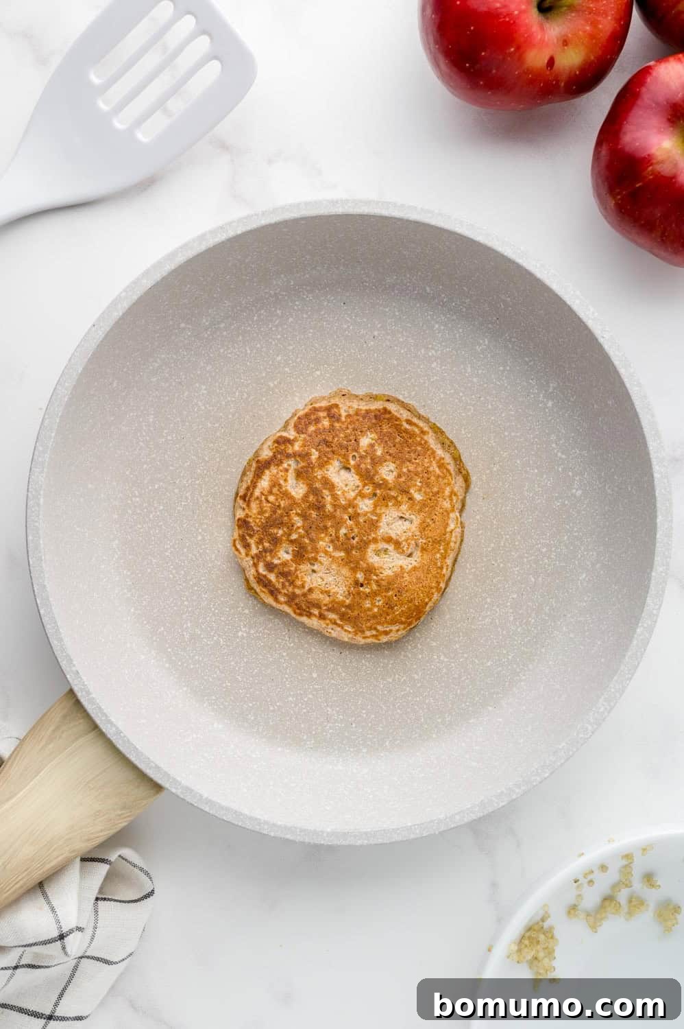 A perfectly cooked apple quinoa pancake with golden-brown edges in the skillet.