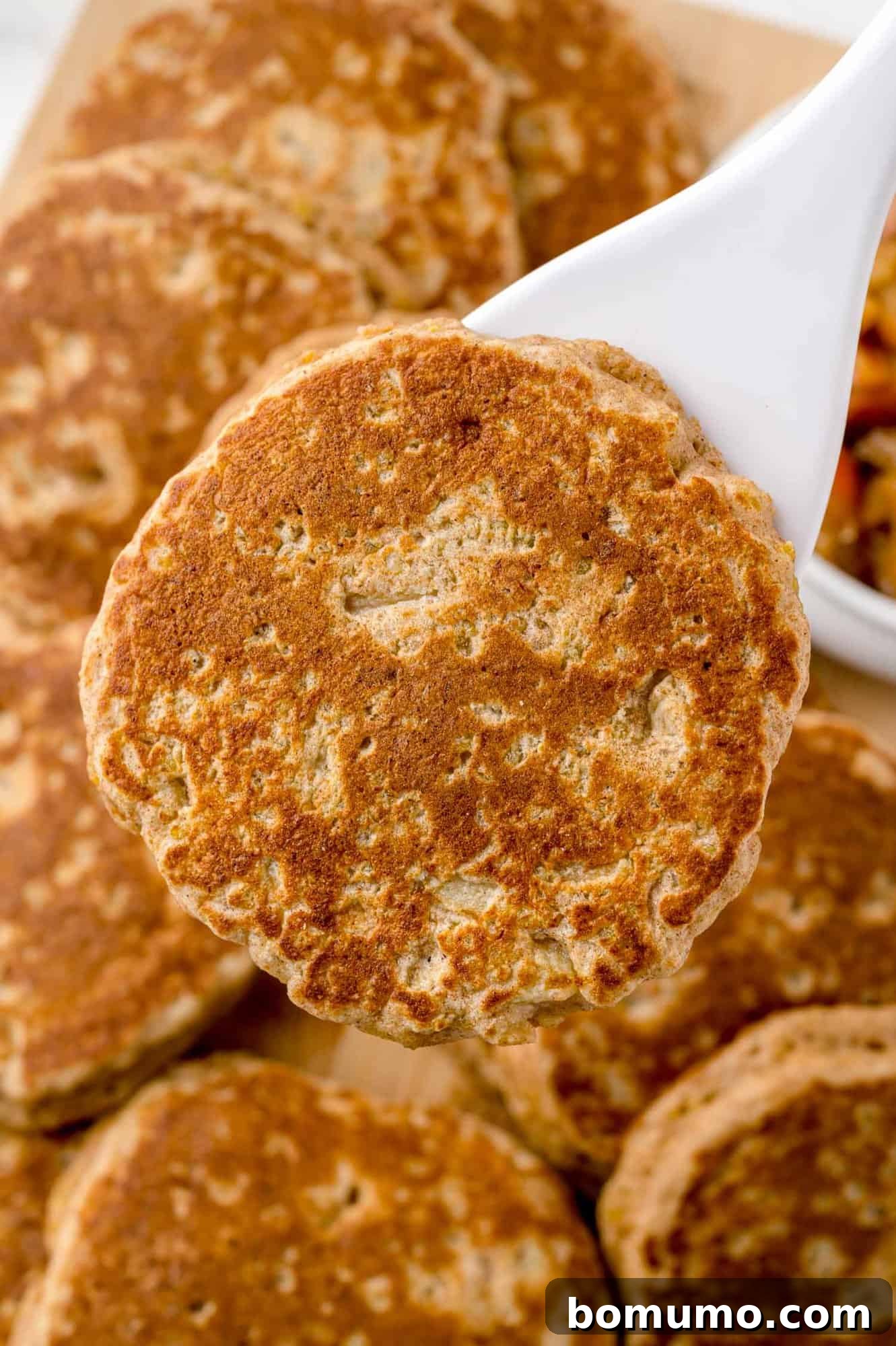 A perfectly golden-brown apple quinoa pancake being lifted from the griddle with a spatula.