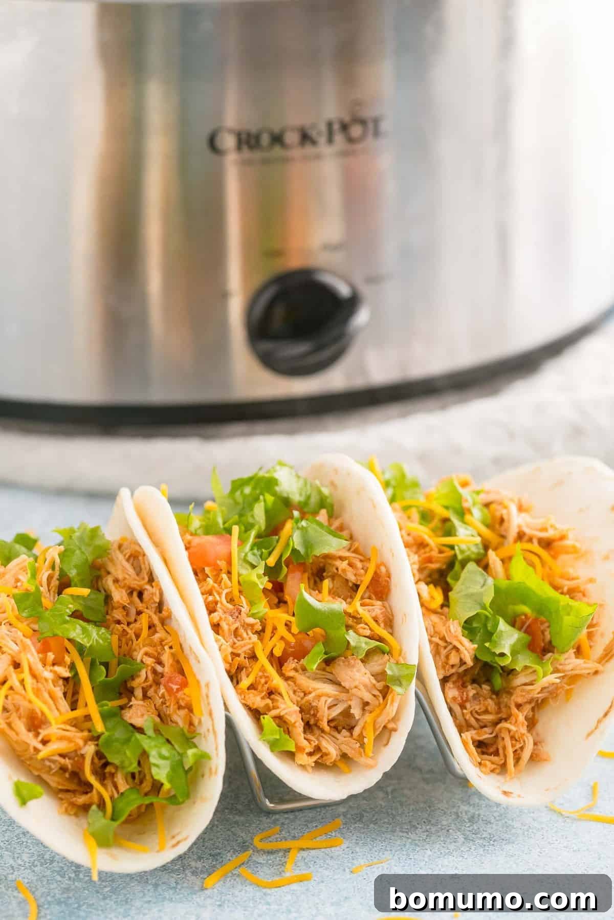 Three soft chicken tacos in front of a crockpot.