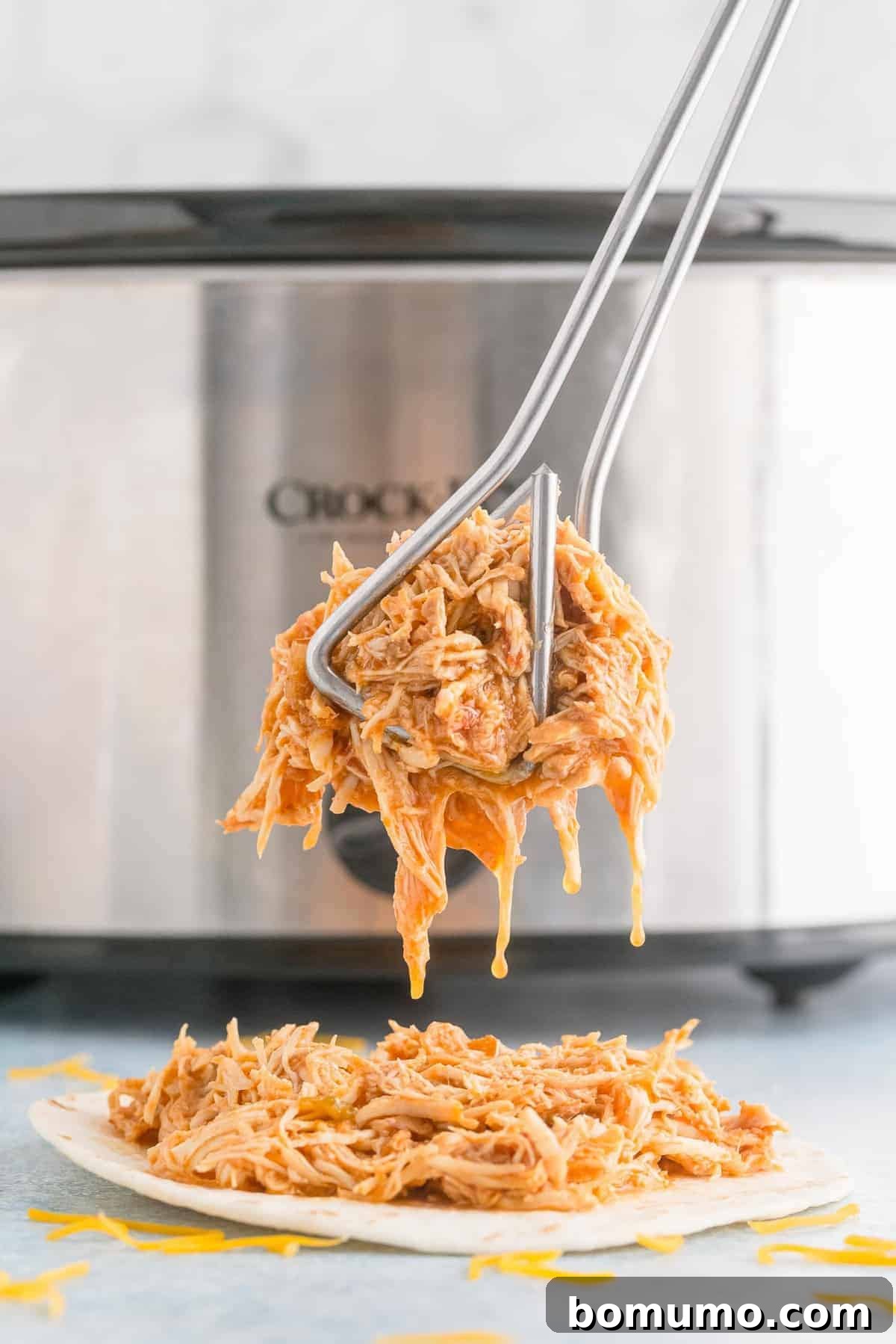 Shredded chicken in tongs in front of a crockpot.