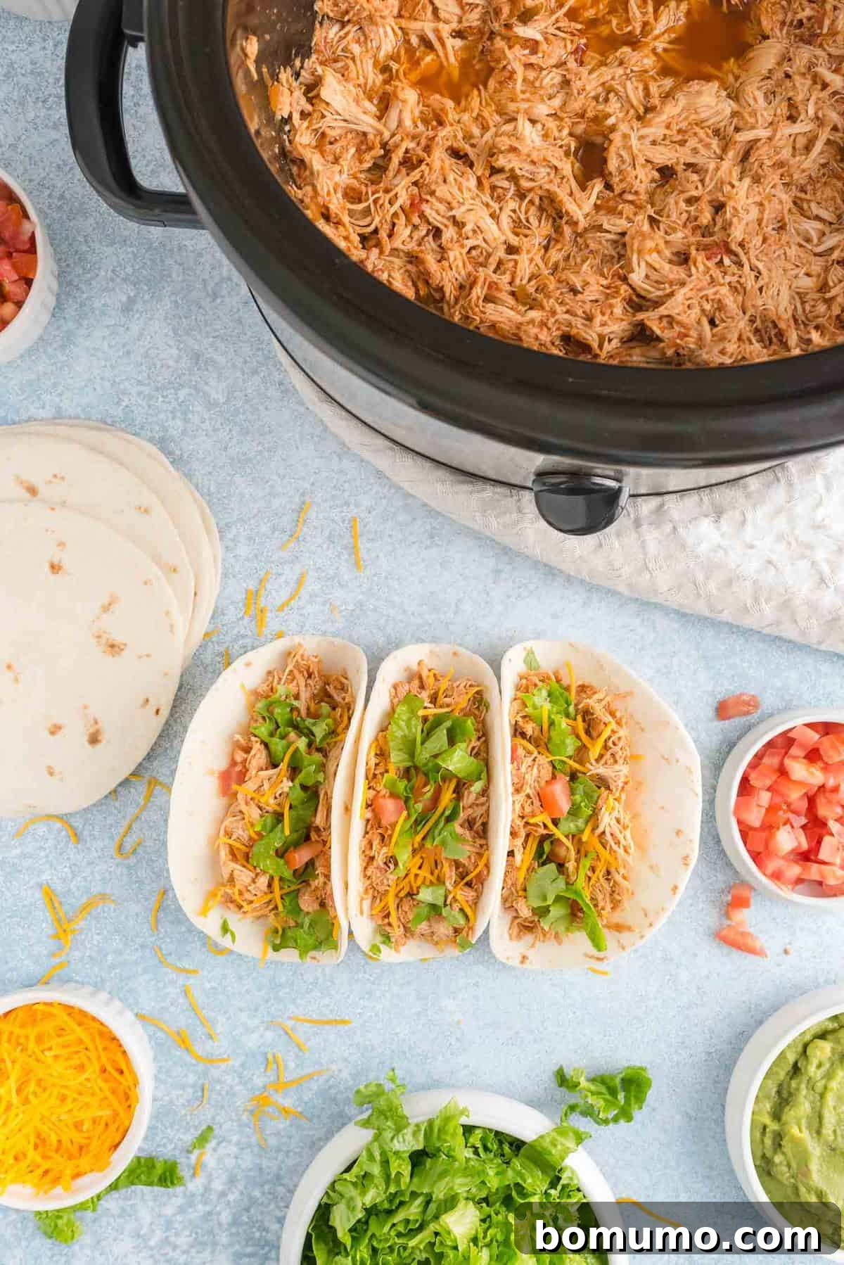 Overhead view of crockpot taco chicken, some in slow cooker and some composed in tacos.
