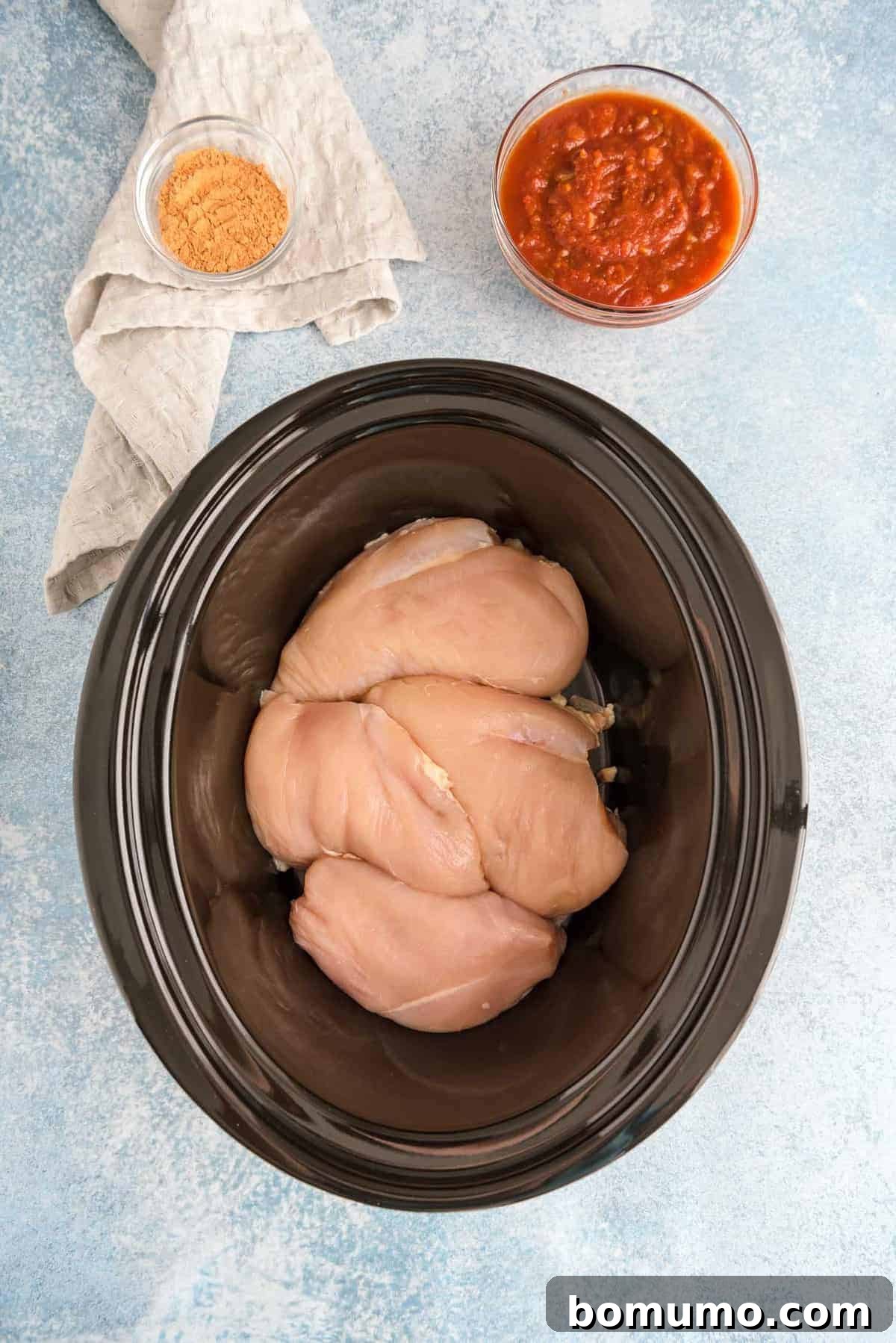 Raw chicken breasts in a black slow cooker.