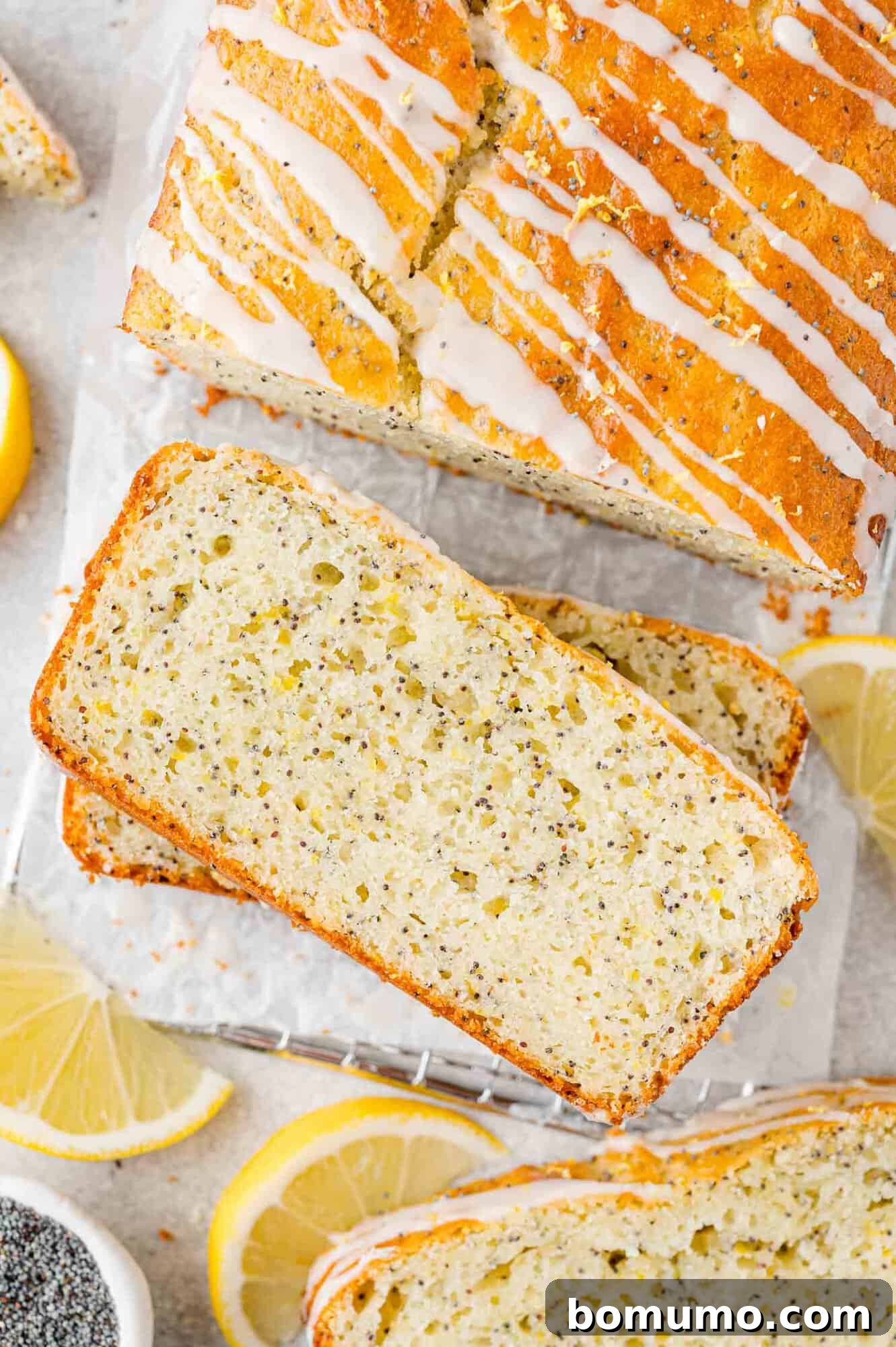 A freshly baked loaf of lemon poppy seed bread, partially sliced, showcasing its moist interior and a delicate lemon glaze drizzled over the top.