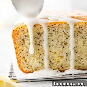 Glistening lemon glaze being artistically drizzled over the top of a golden-brown lemon poppy seed bread loaf, creating an inviting finish.