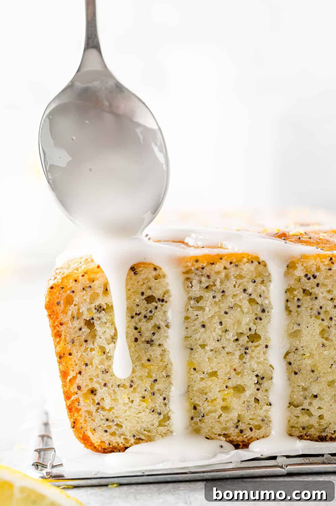 Close-up of a hand drizzling glistening lemon glaze over a fresh loaf of lemon poppy seed bread, creating a beautiful finish.