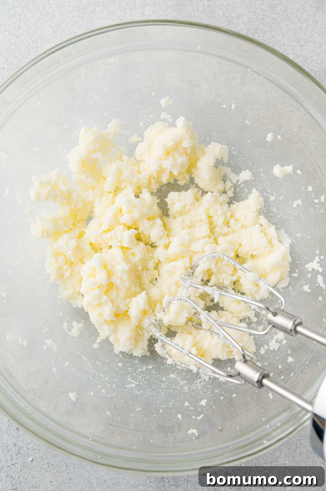 Close-up of butter and granulated sugar being creamed together in a mixing bowl with an electric mixer, showing the developing light and fluffy texture.