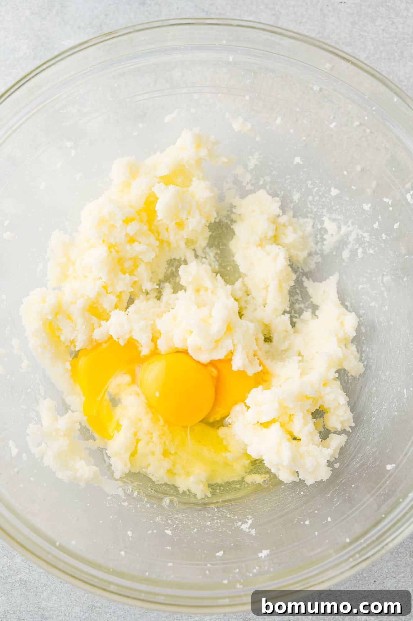 A cracked egg being added to the creamy butter and sugar mixture in a bowl, ready to be beaten in.